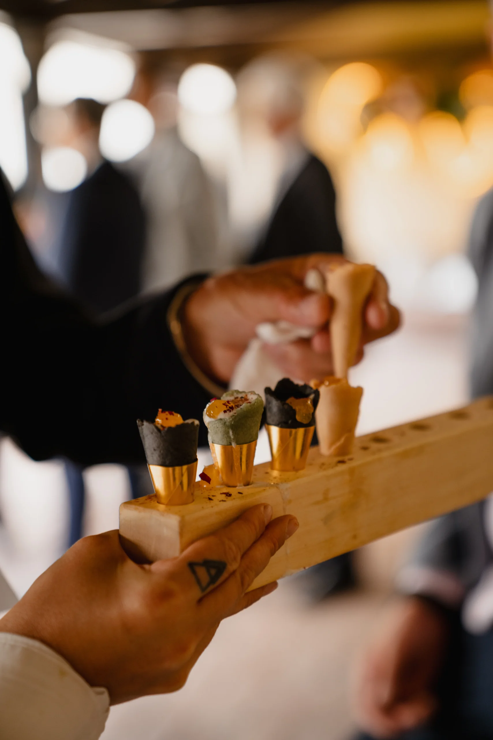 Mano de una camarera sujetando una bandeja con apetitivos en forma de cono mientras un invitado está cogiendo uno