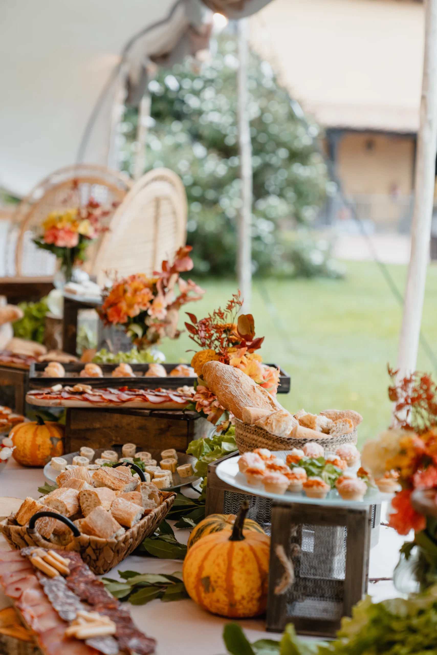 Mesa de aperitivos de embutido variado con pan y decorado con calabazas, cajas de madera y ramos de flores