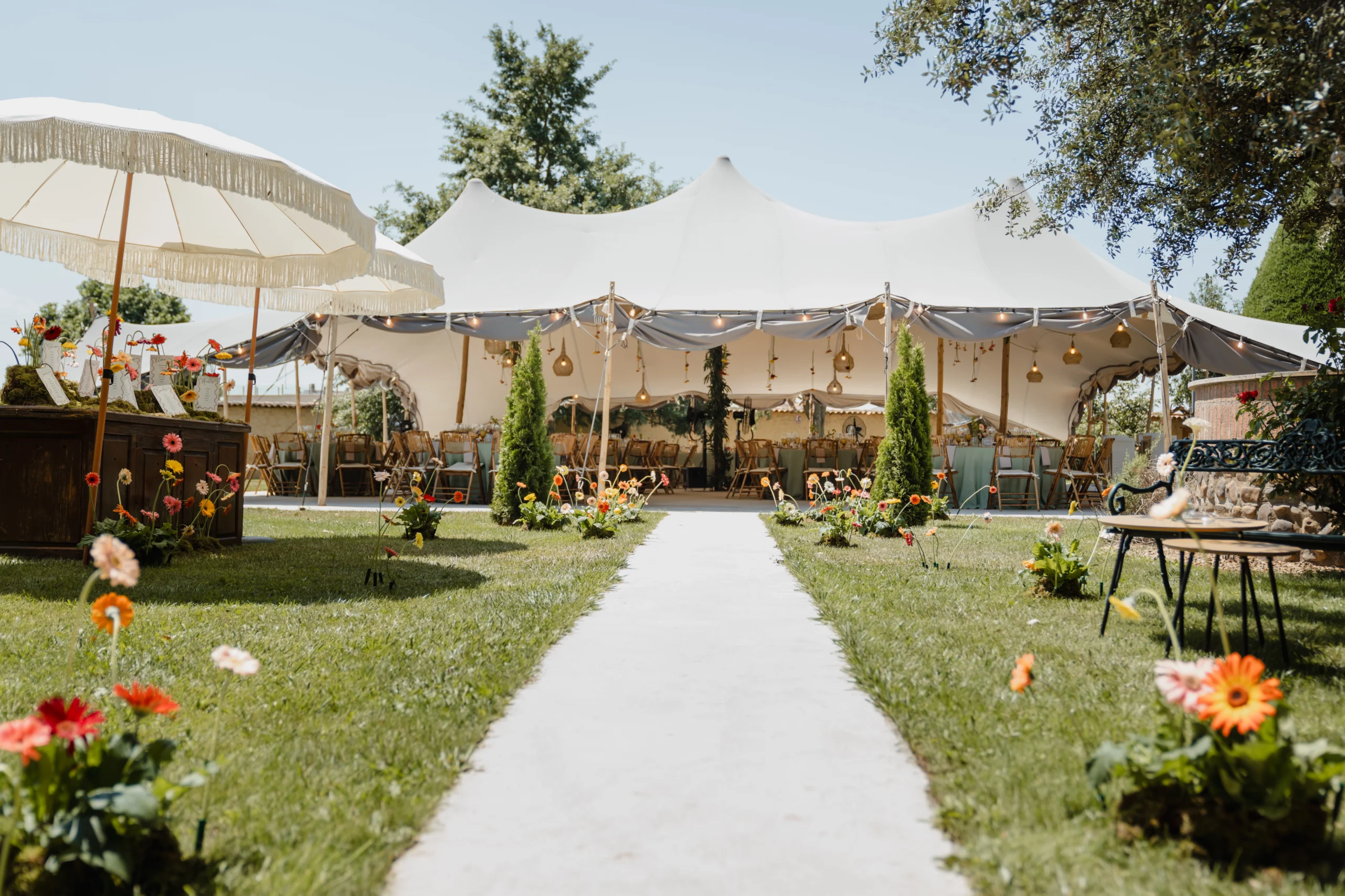 Camino hacia una carpa decorado para una evento con flores, sombrillas y lámparas